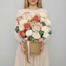 Композиция в шляпной коробке с кофейными розами, кремовыми гвоздиками и хлопком.